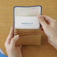 Person holding a brown cardholder with a visible brand name on a wooden surface